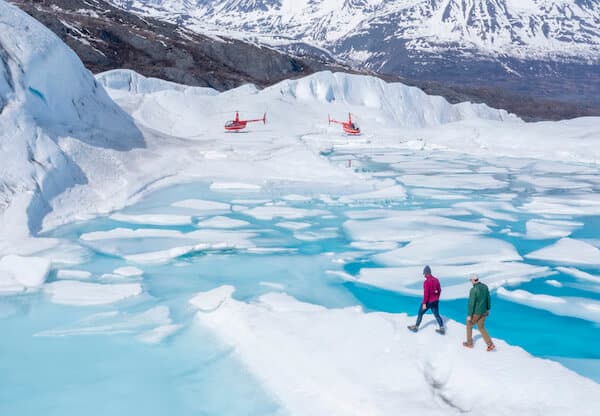 People walking on glacier in Alaska with helicopters